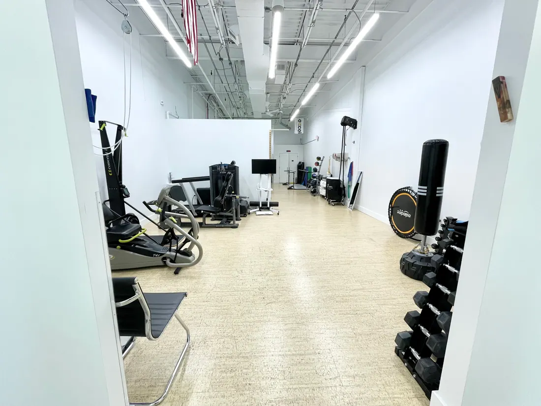 The length of the gym floor, with strength machines and a dumbbell rack