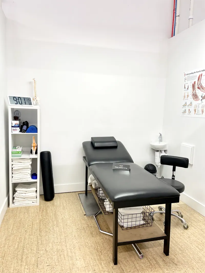A private treatment room with a treatment table, fresh towels on the shelf and an anatomy chart on the wall